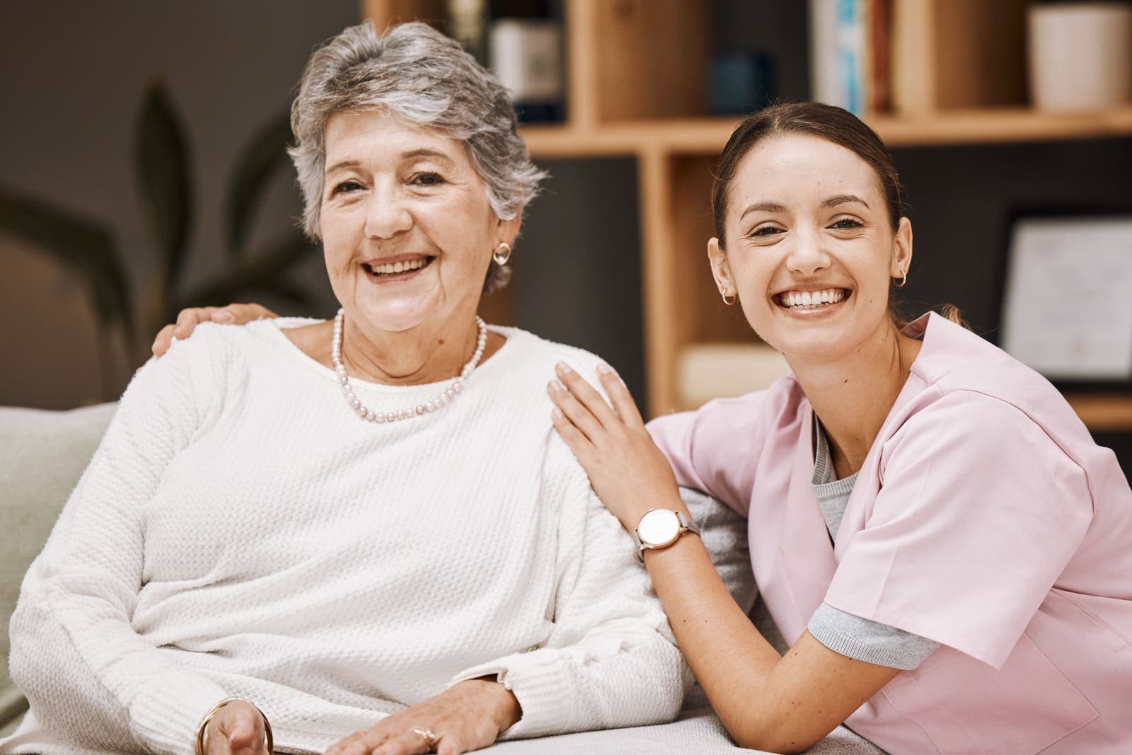 Cuidadora y mujer mayor sonriendo en el salón de casa