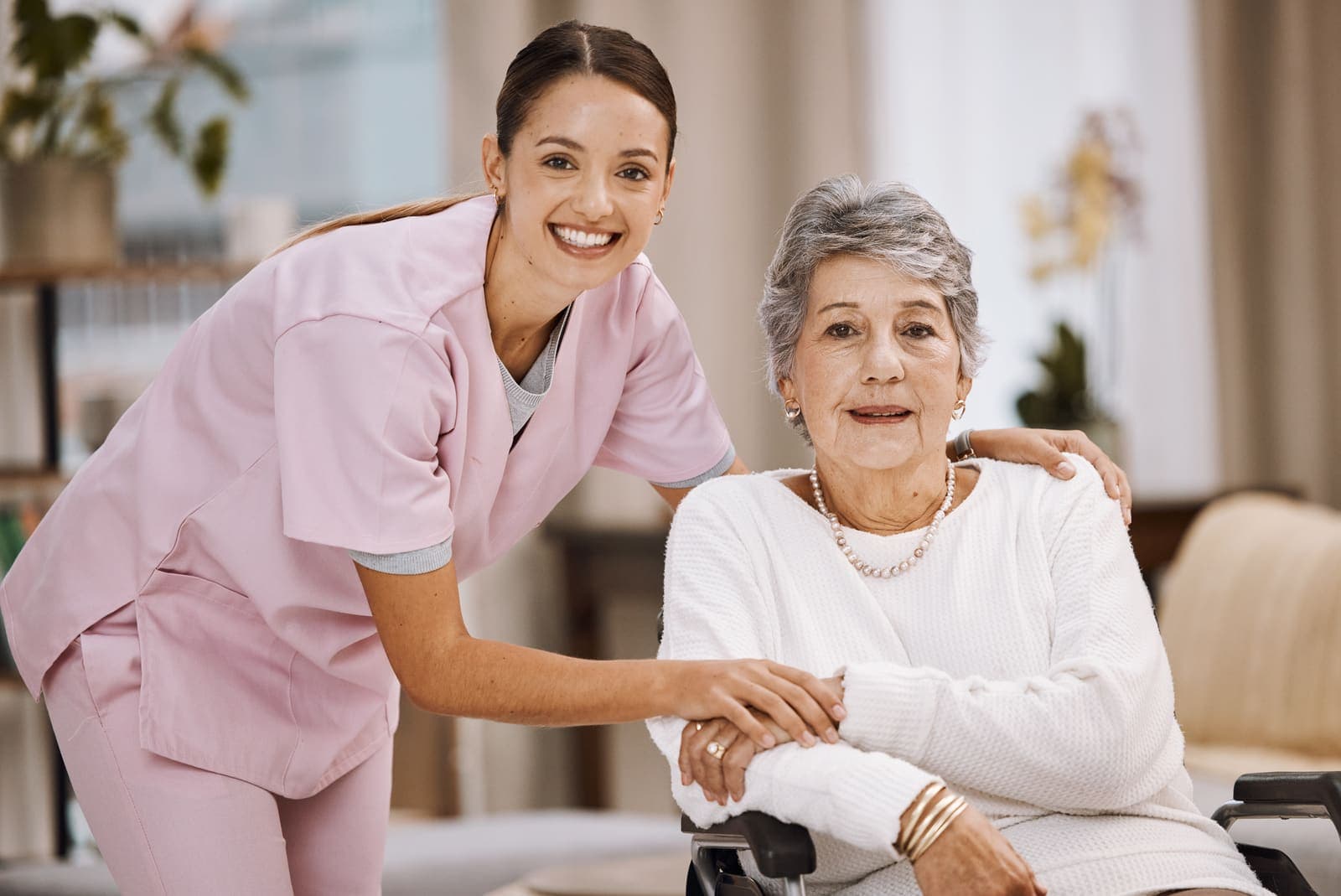 Cuidadora sonriendo junto a una mujer mayor en silla de ruedas